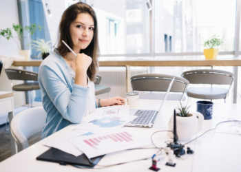 Mulher trabalhando em um computador e analisando gráficos em papéis